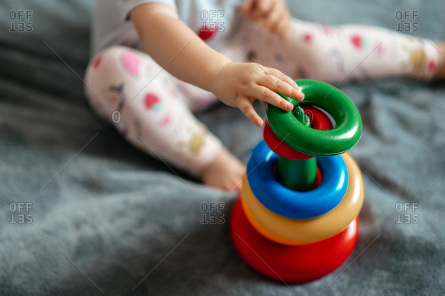 Close-up photo of a little baby who folds a children's multi-colored pyramid sitting on a sofa at home. Top view