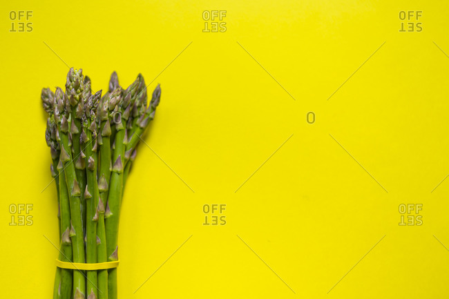 High angle view of green asparagus bunch tied with a yellow rubber band on yellow surface
