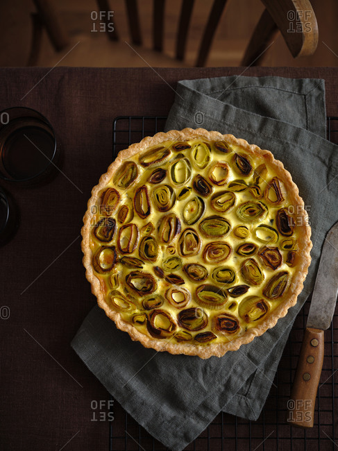Top view of savory cheese and leek tart on dark brown linen tablecloth