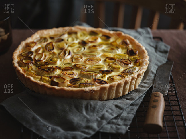 Close up view of rustic homemade leek and cheese tart on a cooling rack on dark linen tablecloth