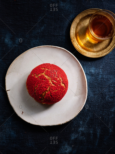 Red raspberry profiterole on beautiful ceramic plate with a cup of tea on dark textile background