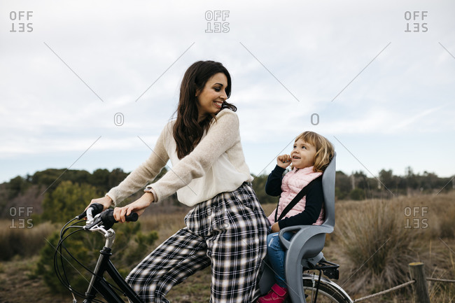 Woman riding bicycle in the countryside with daughter in child's seat