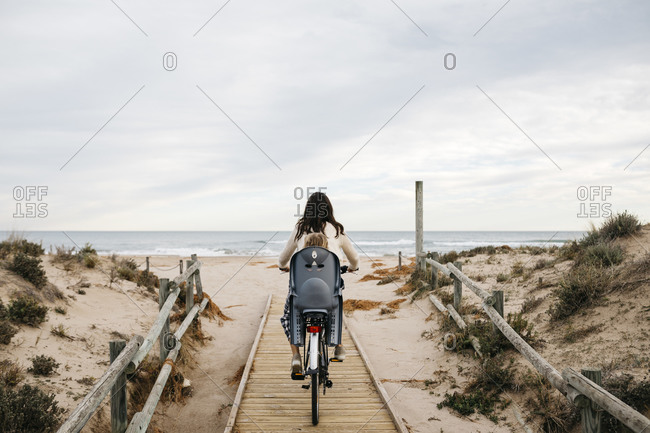 Woman riding bicycle on a boardwalk in the dunes with daughter in child's seat