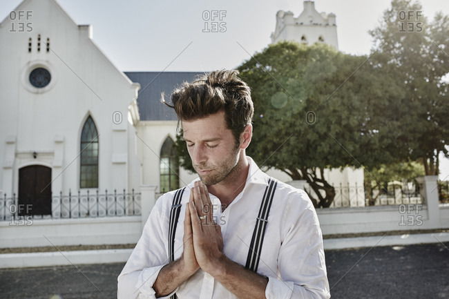 Portrait of man in old-fashioned clothes in the countryside praying at a church