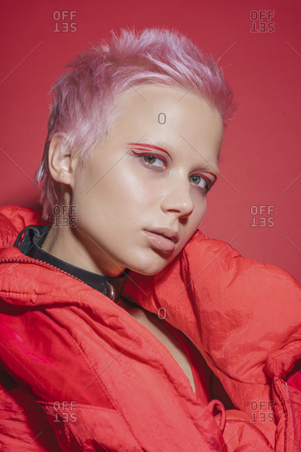 Portrait of young woman with short pink hair wearing red jacket in front of red background