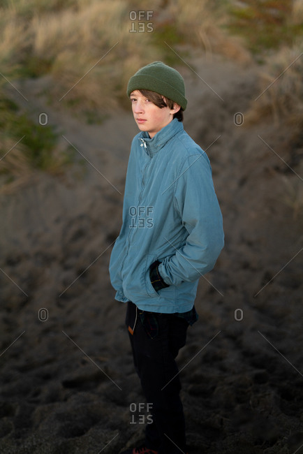 Teenage boy standing at the base of a dune on the coast at twilight