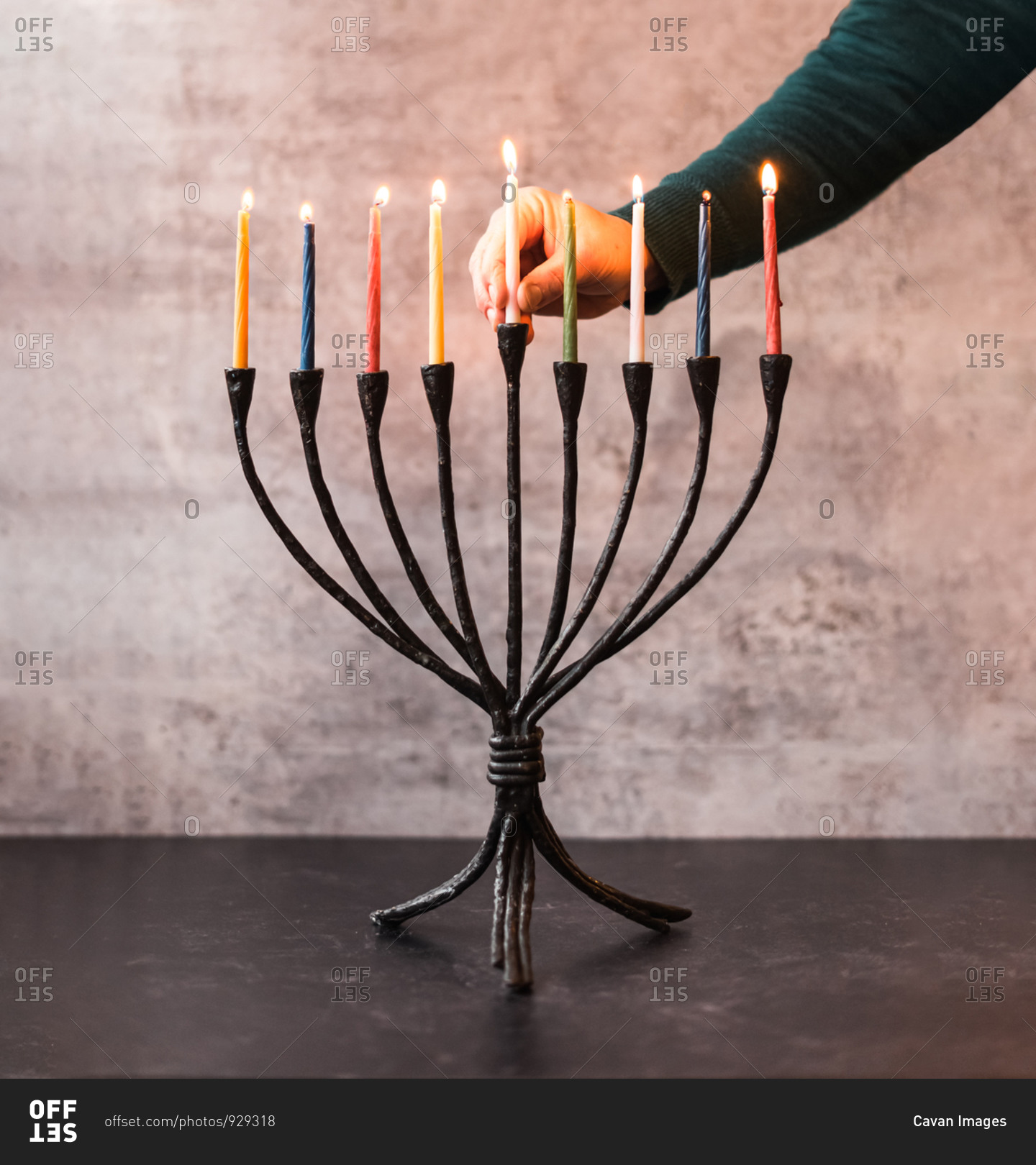 Woman\'s hand placing a lit candle in a menorah for Hanukkah.
