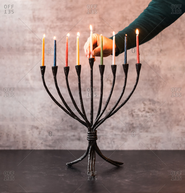 Woman\'s hand placing a lit candle in a menorah for Hanukkah.