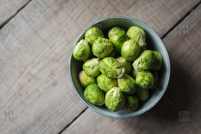 Overhead view of bowl of Brussels sprouts on wooden background.