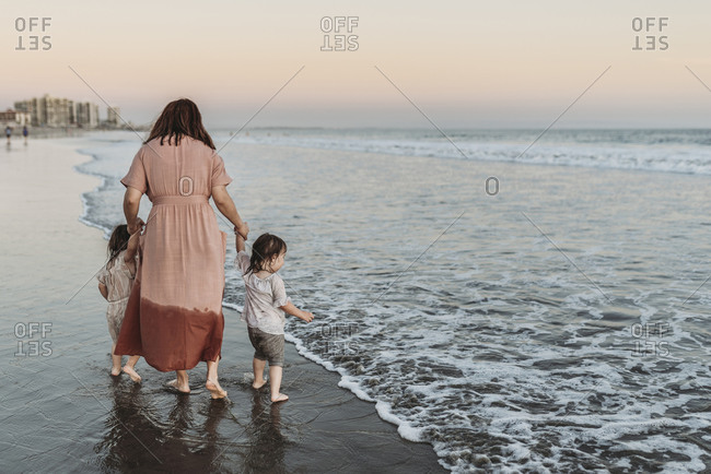 Behind view of mother walking young daughters in ocean at beach