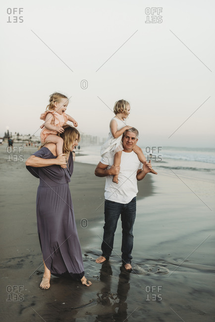 Lifestyle image of mother and father holding young daughters on should