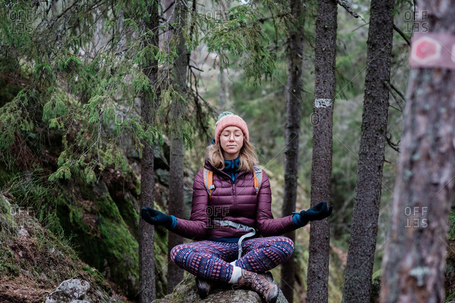 Woman solo hiking whilst meditating on a rock in a forest