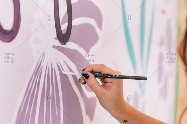 A close up of a painter at work and painting florals on a wall.