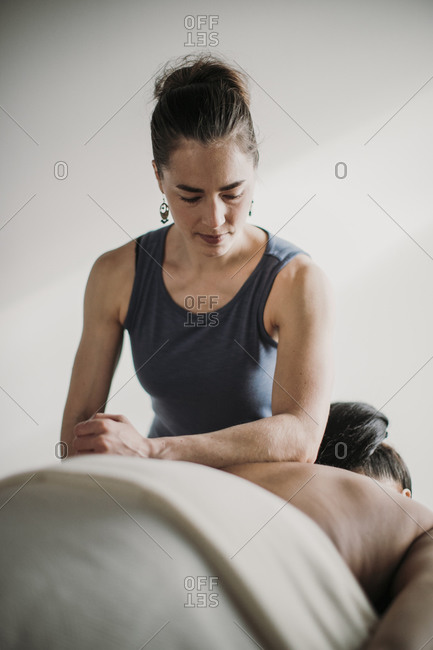 Female massage therapist treat female patient indoors on massage table