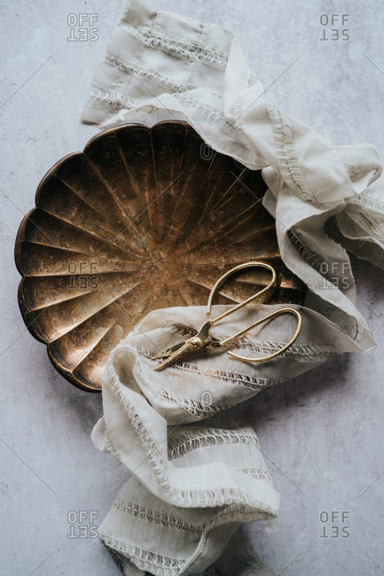 Vintage fabrics draped around bowl on concrete with old tray and scissors