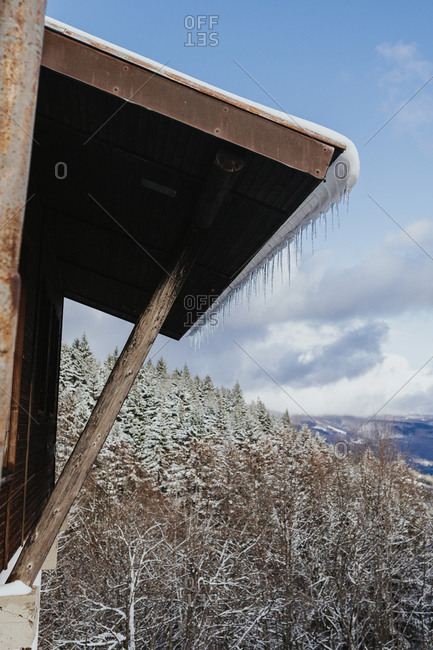 Icicles line the roof of a traditional mountain hut with a pine forest in the background