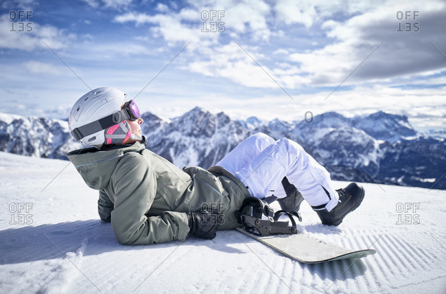 Smiling woman sitting with snowboard on viewpoint and enjoying view at distance