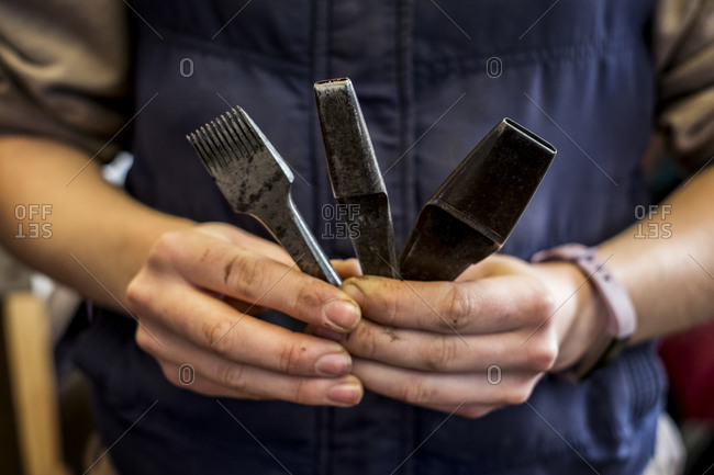 Close up of person holding three metal saddle making tools.