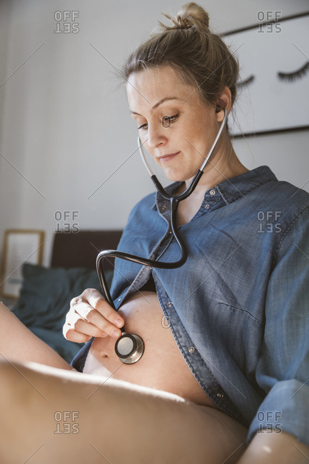 Pregnant woman holding a stethoscope to hear the heartbeat of her baby