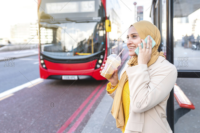 Portrait of smiling young woman on the phone waiting at bus stop