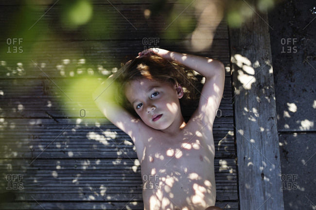 Overhead view of young boy lying shirtless on a wooden deck