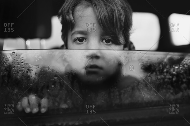 Young boy looking out wet car window with sad expression