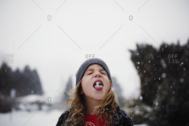 Young boy with long curly hair catching snowflakes on his tongue