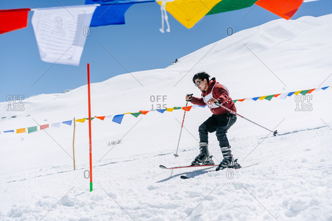 Spiti, Himachal Pradesh, India - April 1, 2019: Man skiing down snowy hill with Tibetan prayer flags