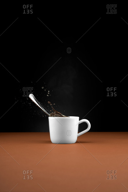 White ceramic cup with spoon and splashing hot beverage