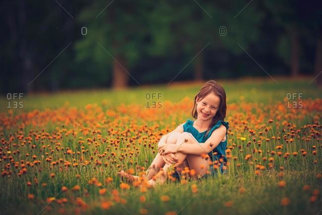 Happy girl sitting in a meadow with wildflowers laughing, USA