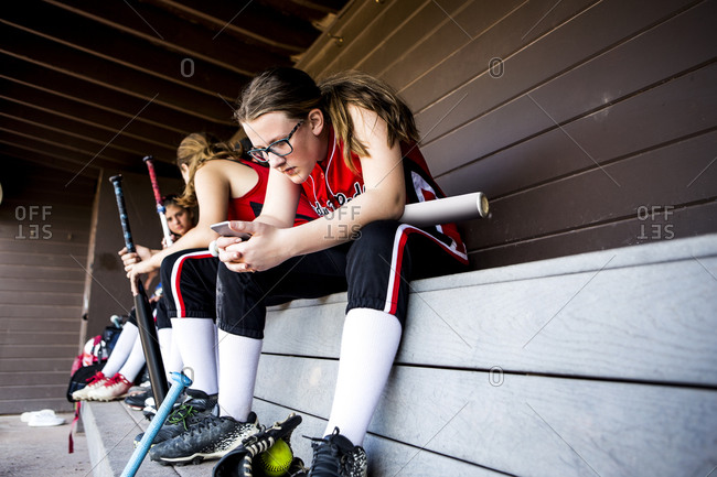 Young female softball player looking at mobile phone in dugout