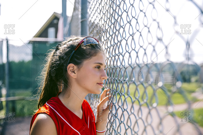 Portrait of middle school softball player standing near fence in dugout