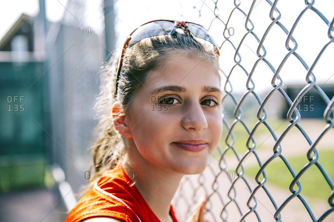 Portrait of middle school softball player standing near fence in dugout