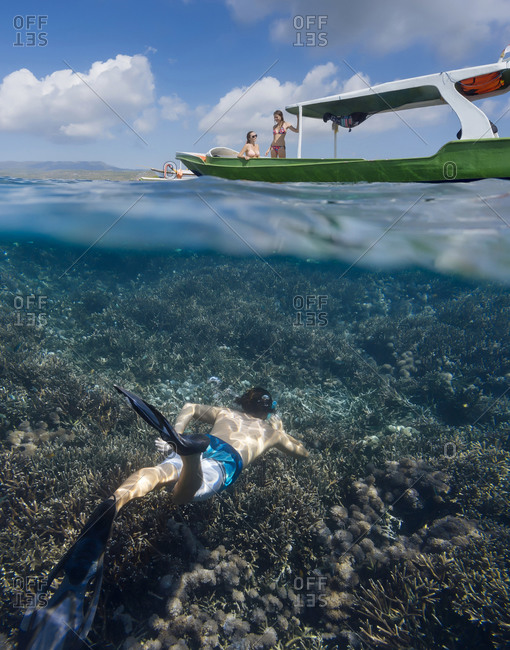 Young man snorkeling near the boat in ocean, underwater view