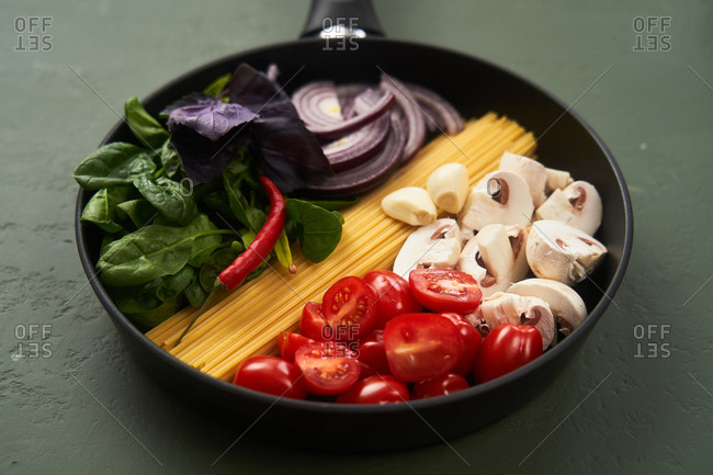 Close up of pasta ingredients in a pan on green textured surface