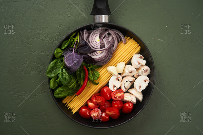 Top view of pasta ingredients in a pan on green textured surface