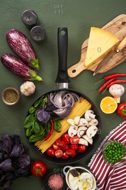 Skillet fillet with and surrounded by pasta ingredients on green textured surface