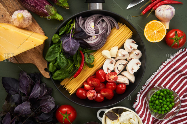 Overhead view of a skillet fillet with and surrounded by pasta ingredients on green textured surface