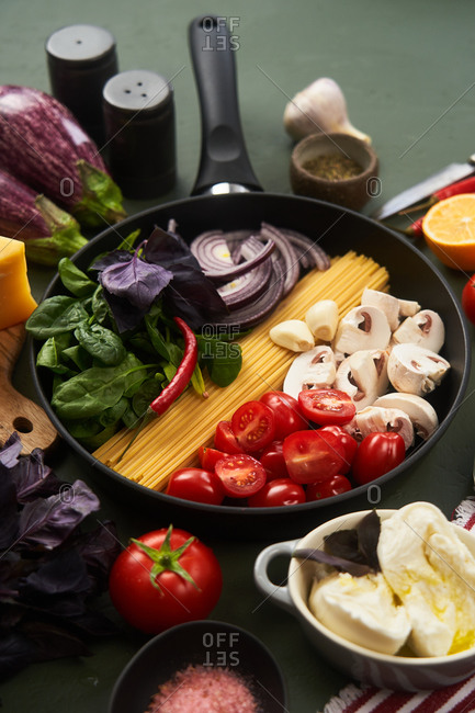 Skillet fillet with fresh ingredients for pasta on green textured surface