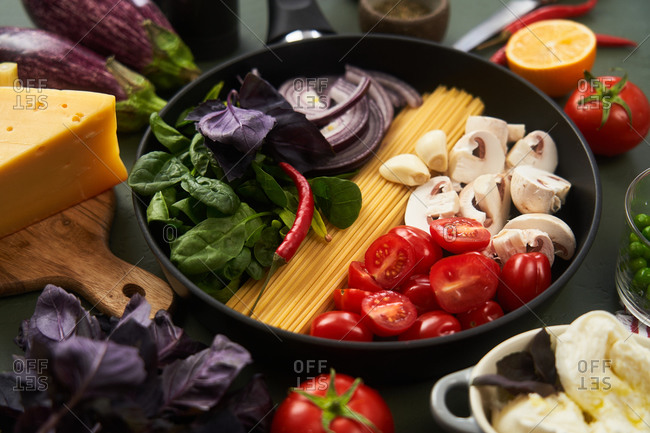 Close up of a skillet fillet with fresh ingredients for pasta on green textured surface