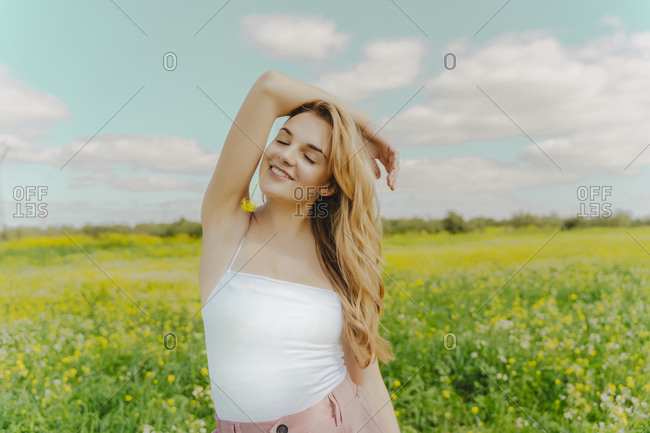 Smiling young woman standing in a flower meadow in spring with blossom in her mouth