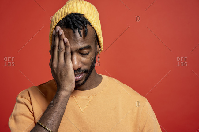 Portrait of stylish young man covering one eye in front of orange wall