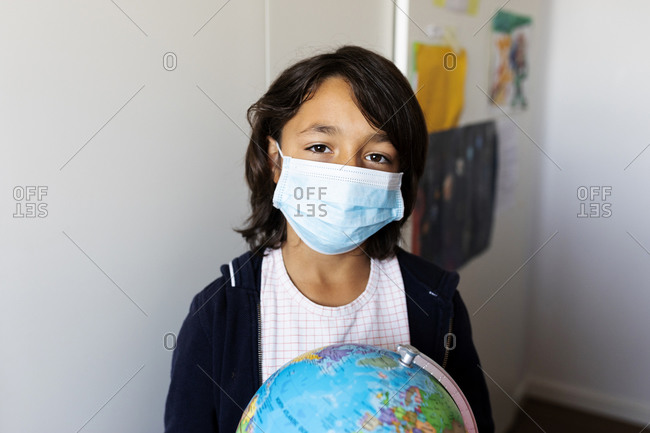 Portrait of a pre-teen in medical mask holding globe