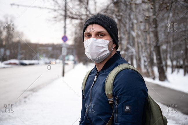 Moscow, Russia - March 31, 2020: Young man waits for a bus wearing a protective mask against the coronavirus