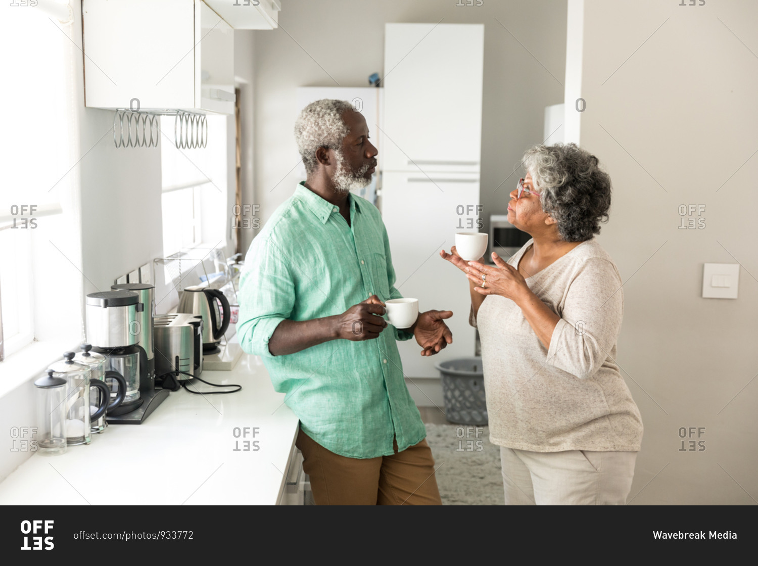 A senior African American couple spending time at home together, social distancing and self isolation in quarantine lockdown during coronavirus covid 19 epidemic, standing in the kitchen, talking, holding cups