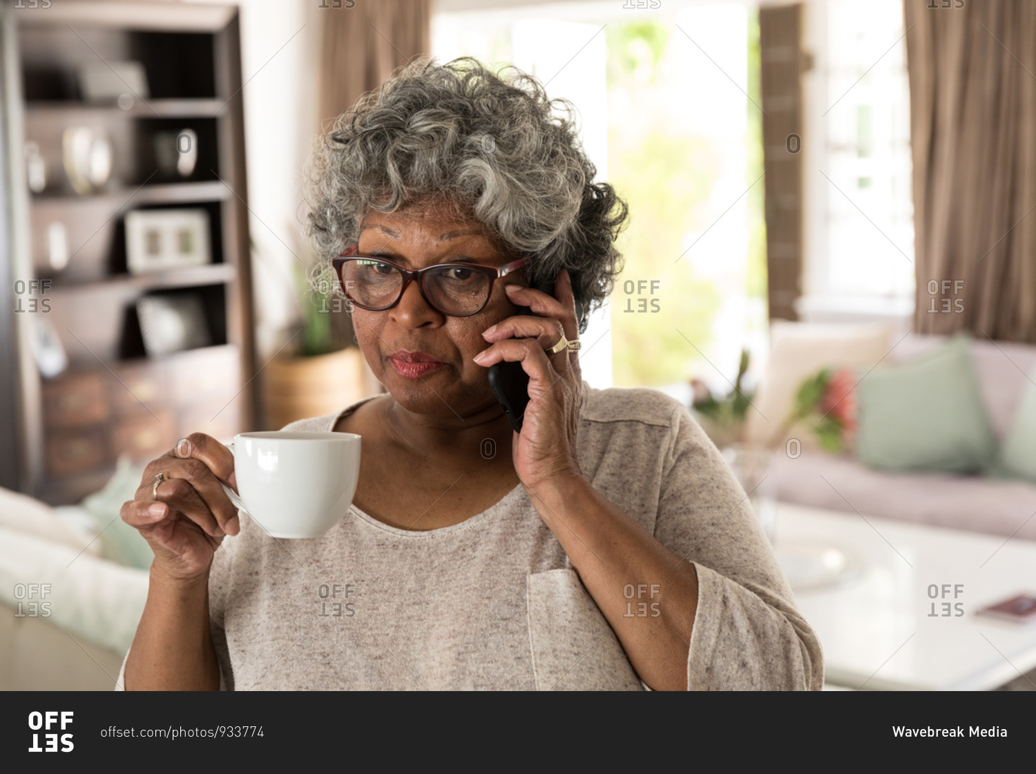 A senior African American woman spending time at home, social distancing and self isolation in quarantine lockdown during coronavirus covid 19 epidemic, talking on a smartphone and holding a cup