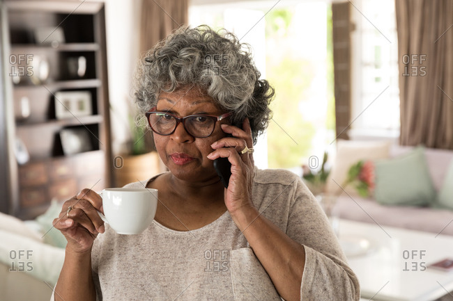 A senior African American woman spending time at home, social distancing and self isolation in quarantine lockdown during coronavirus covid 19 epidemic, talking on a smartphone and holding a cup
