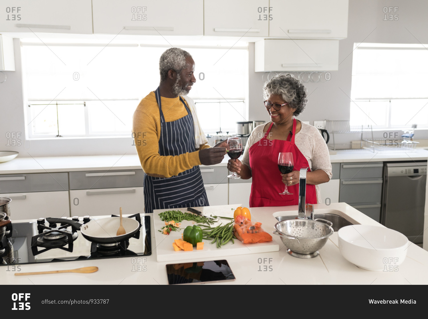 A senior African American couple spending time at home together, social distancing and self isolation in quarantine lockdown during coronavirus covid 19 epidemic, standing in the kitchen preparing food, the woman holding glasses of red wine