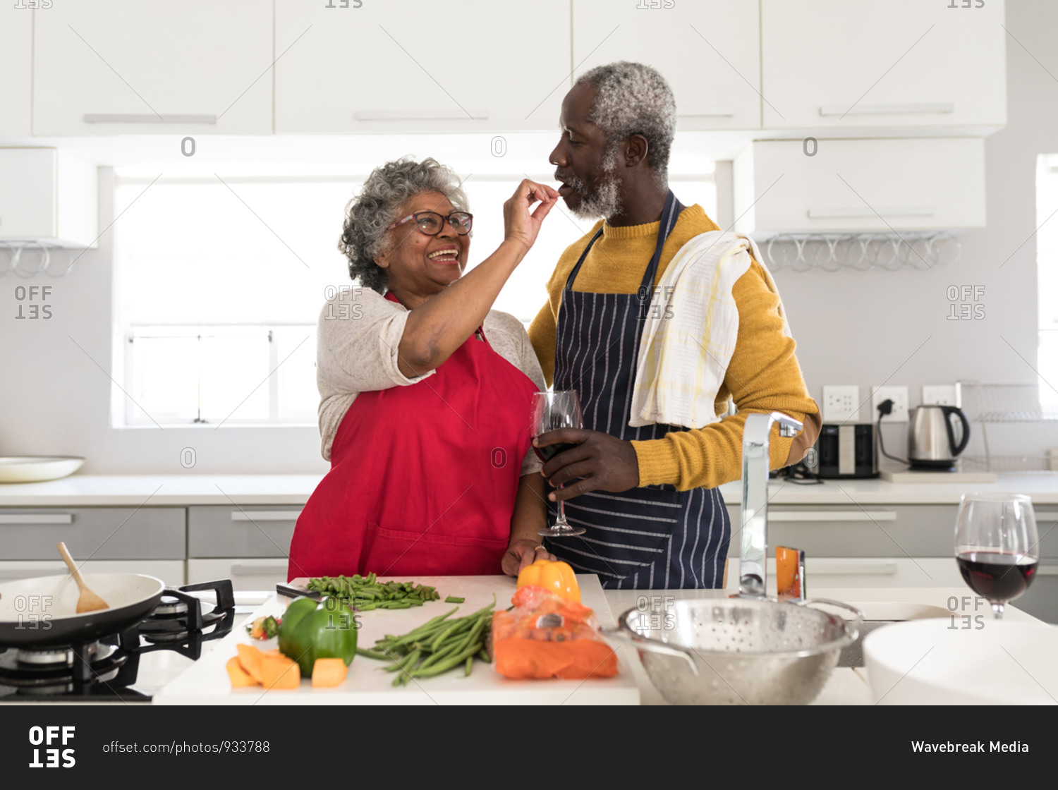 A senior African American couple spending time at home together, social distancing and self isolation in quarantine lockdown during coronavirus covid 19 epidemic, standing in the kitchen preparing food, the man holding glasses of red wine