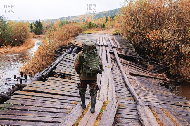 Angler crossing collapsed wooden bridge, Ural, Russia